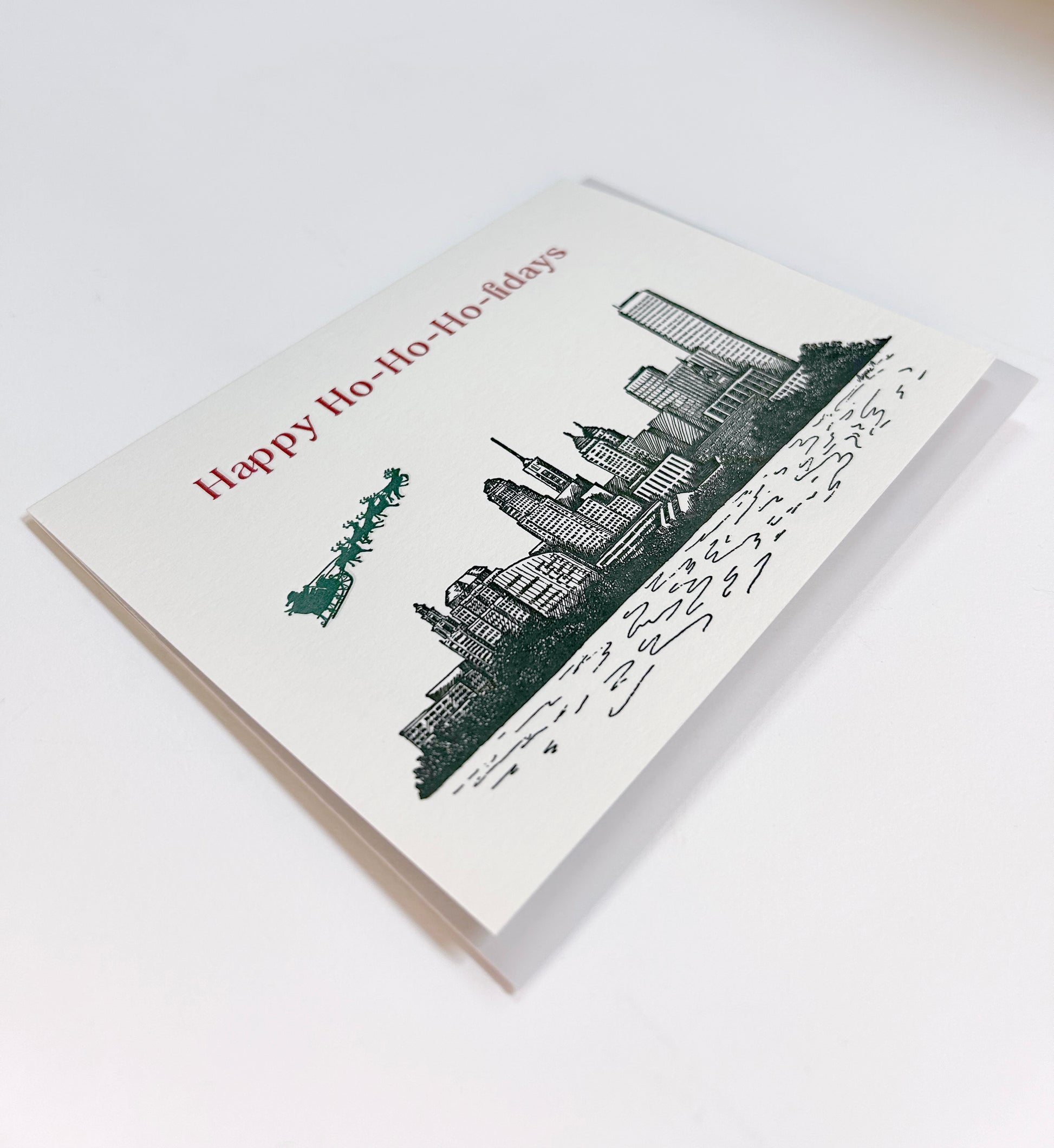 Letterpress card with city skyline and Santa/ reindeer flying over that reads Happy Ho-Ho-Ho-lidays" by Rust Belt Love.