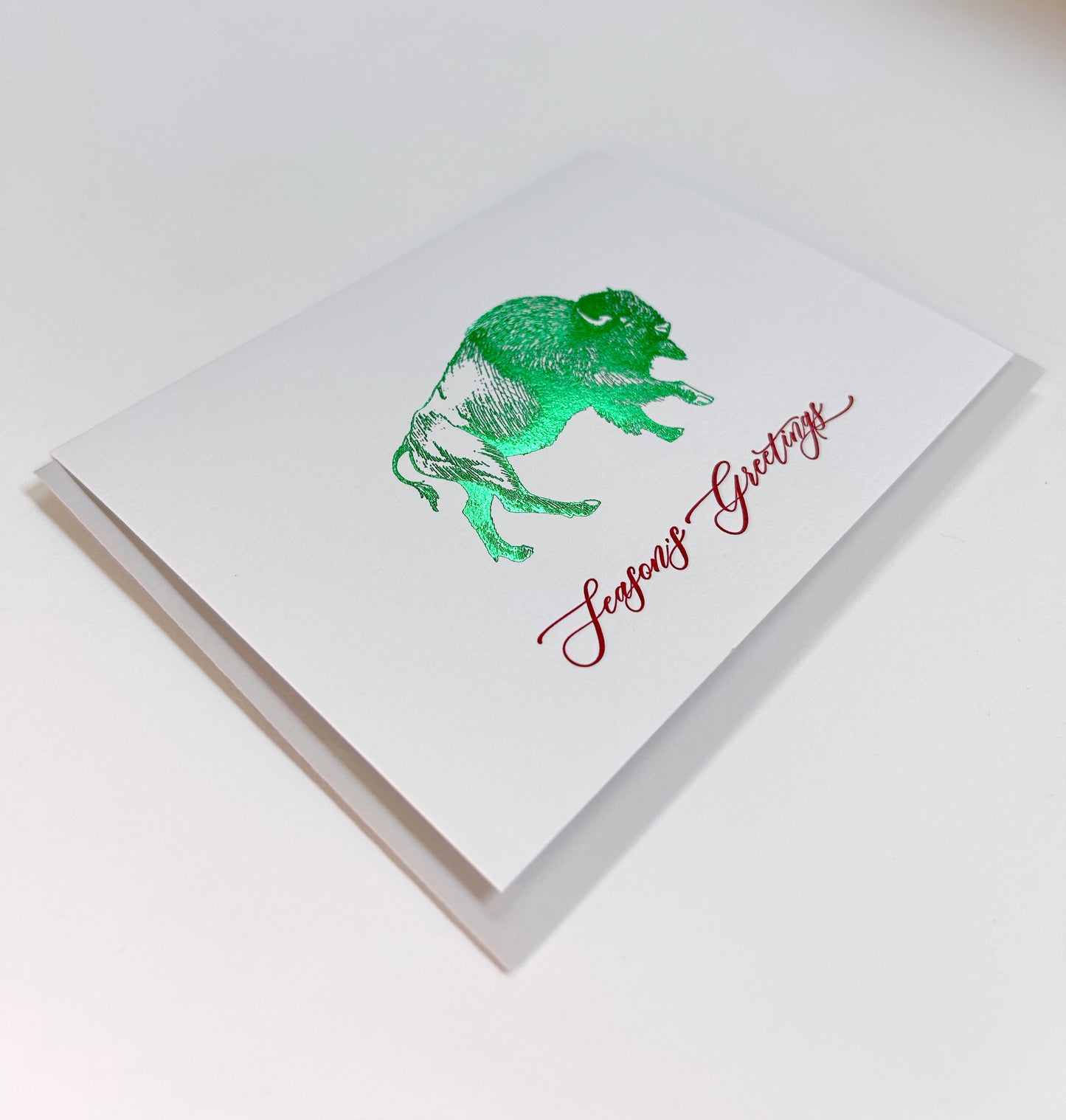 Letterpress and green foil buffalo greeting card that reads "Season's greetings" in red ink, by Rust Belt Love