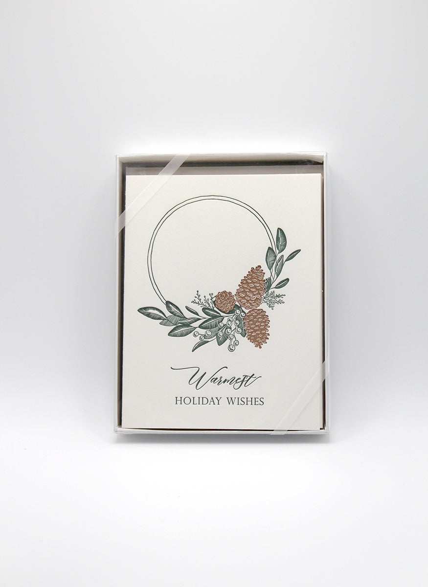 Box of letterpress holiday cards with pinecones and greenery that says "Warmest holiday wishes" by Rust Belt Love