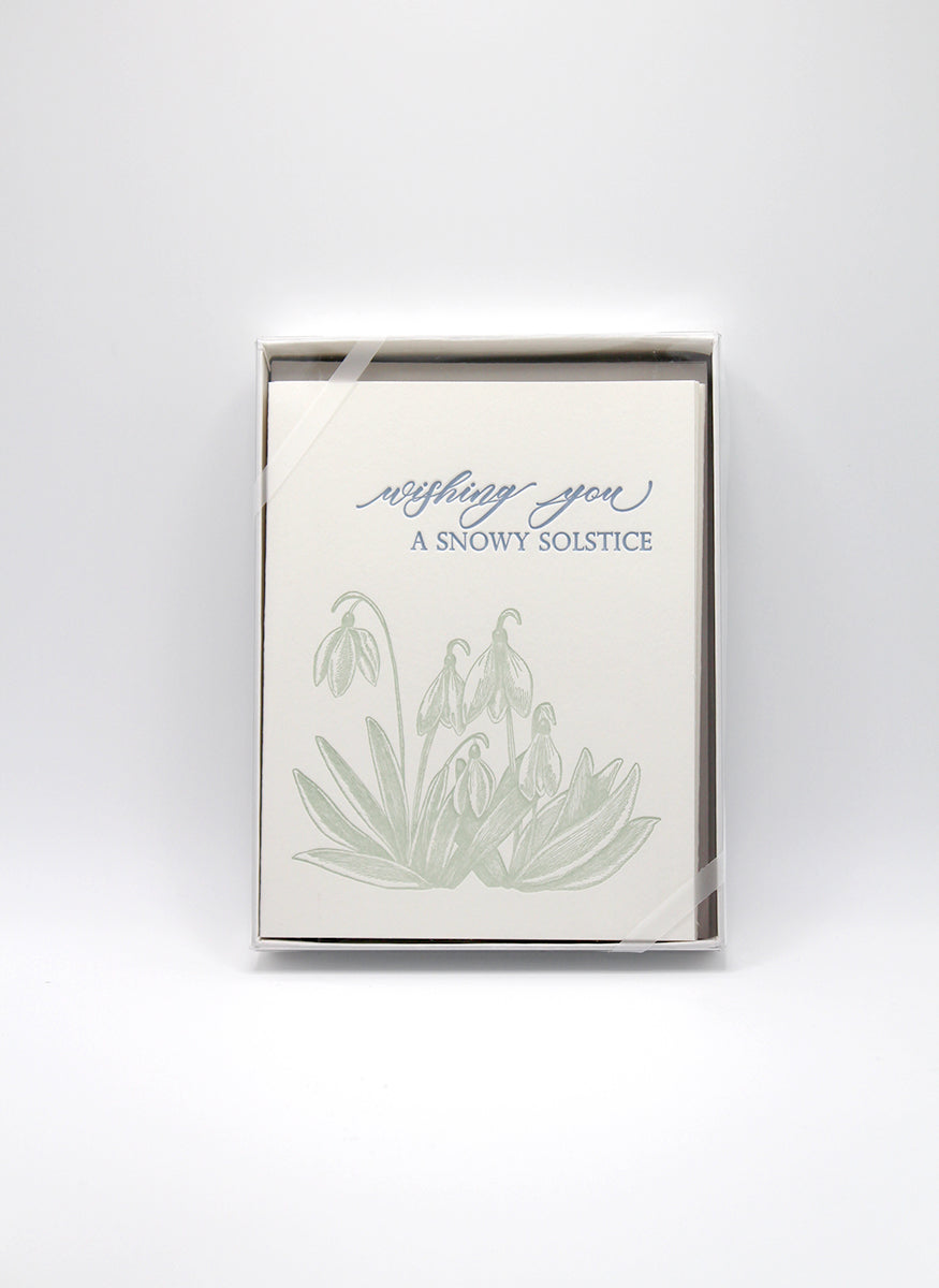 Box of letterpress holiday cards with snowdrop flowers that says "Wishing You A Snowy Solstice" by Rust Belt Love