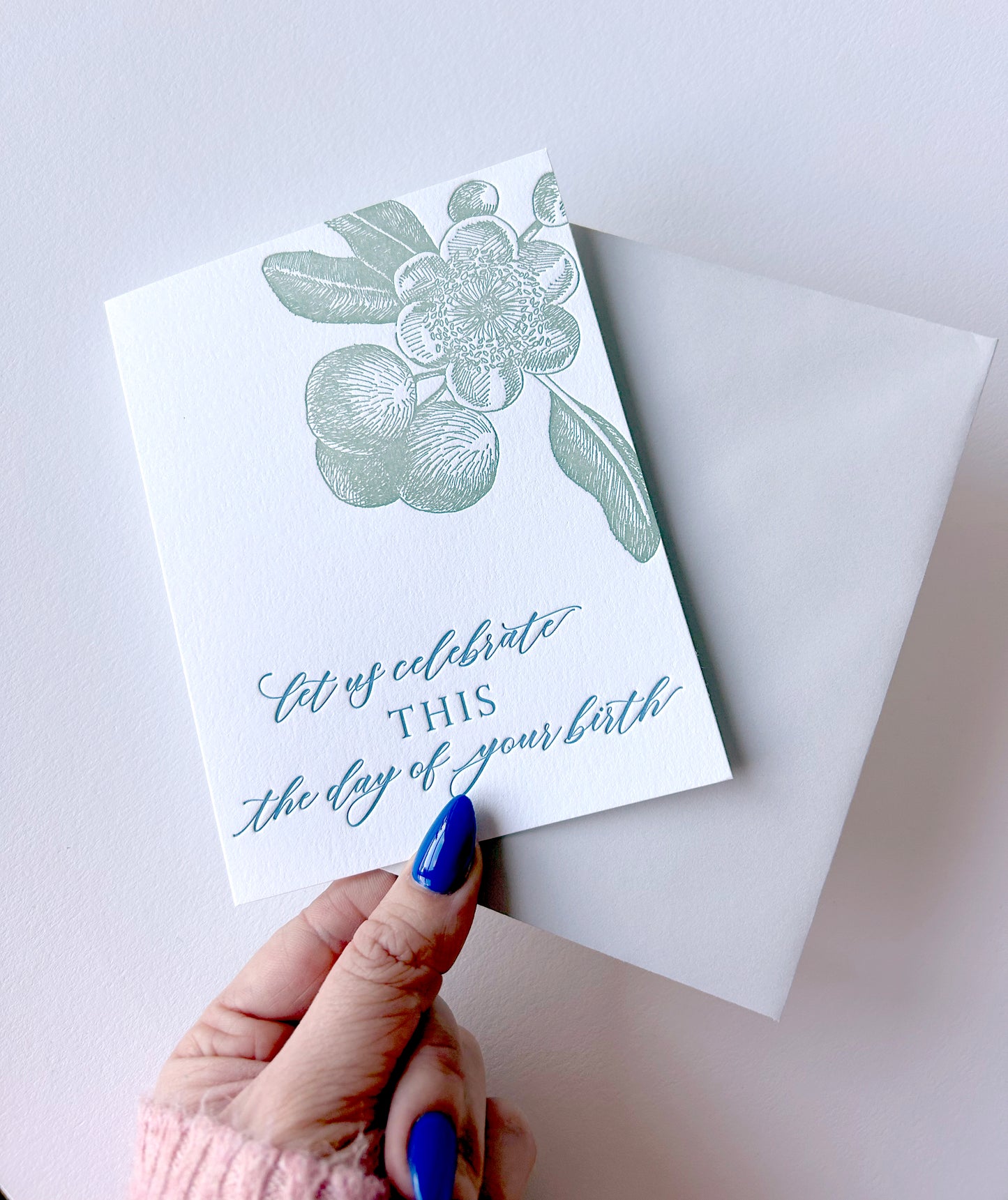 Hand holding letterpress birthday card with florals that says " Let Us Celebrate This The Day Of Your Birth" by Rust Belt Love