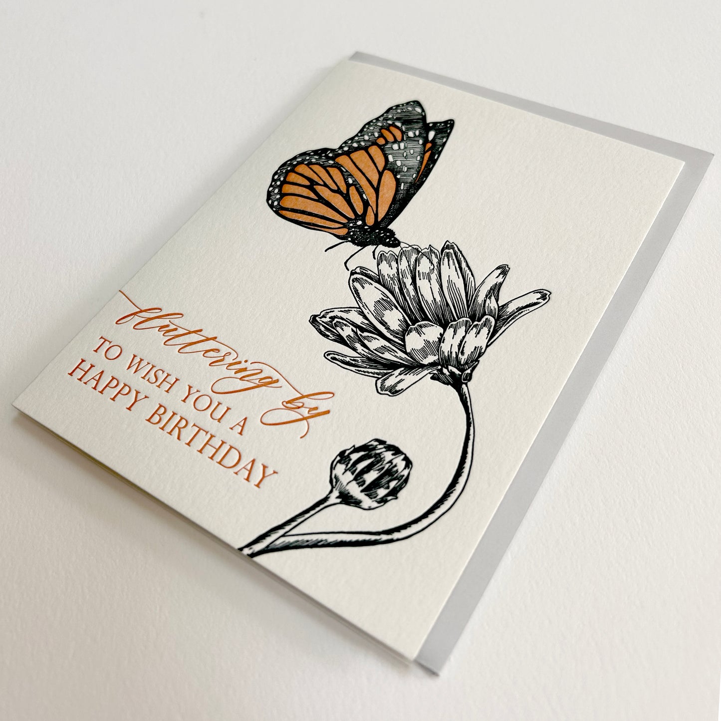 Letterpress birthday greeting card with black and orange ink with a flower and butterfly on it that reads "Fluttering by to wish you a happy birthday", by Rust Belt Love