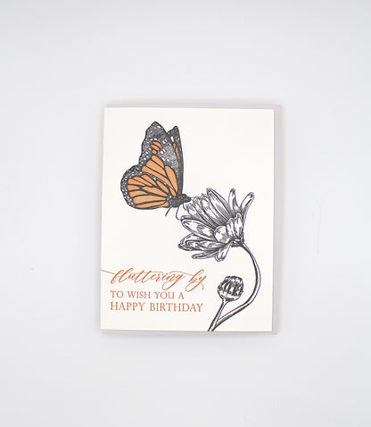Letterpress birthday greeting card with black and orange ink with a flower and butterfly on it that reads "Fluttering by to wish you a happy birthday", by Rust Belt Love