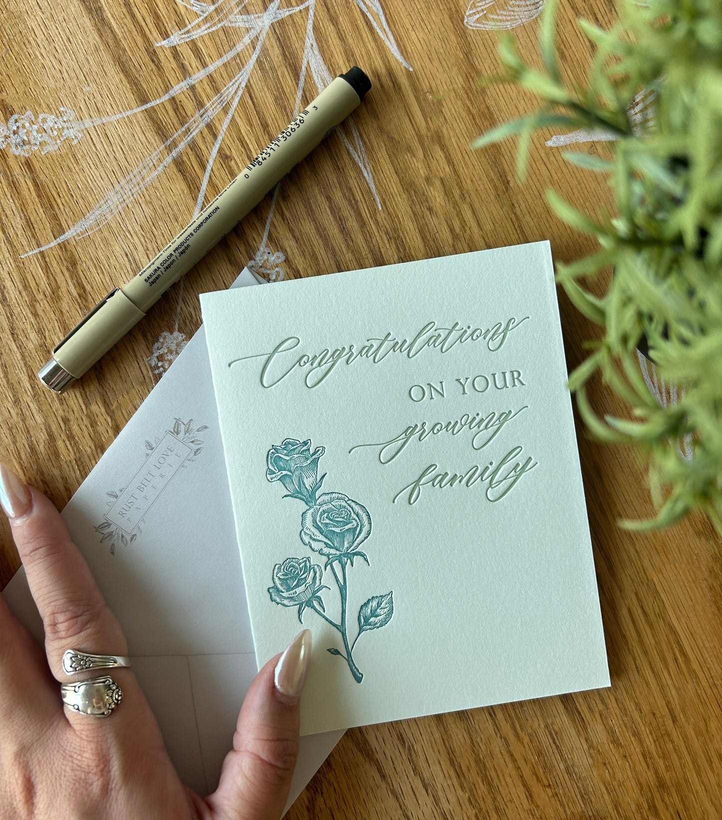 Style shot of green letterpress congrats card with florals that reads "Congratulations on your growing family" by Rust Belt Love