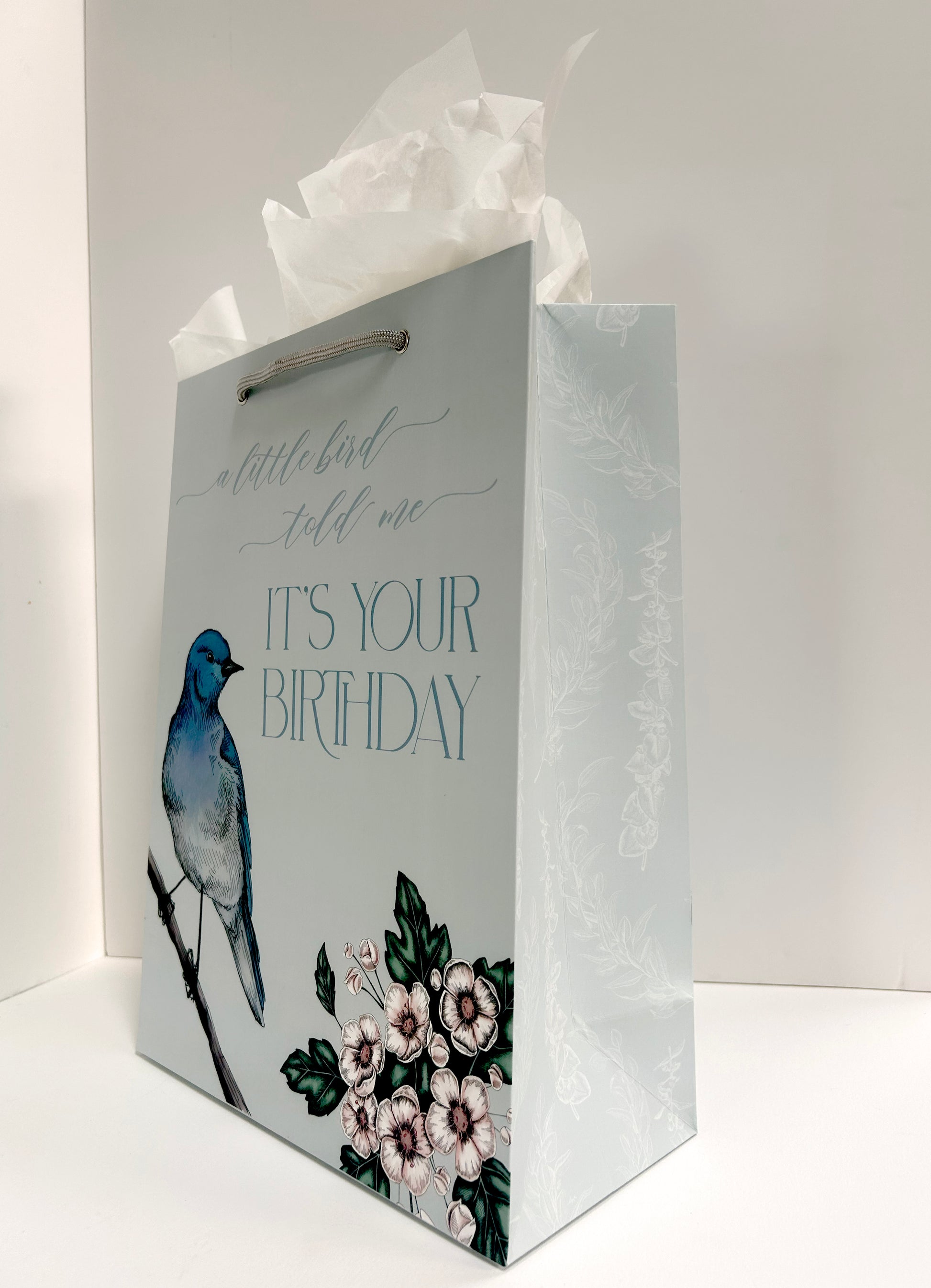  Angled picture of a standing blue birthday gift bag with florals and a bird that reads "A little bird told me it's your birthday" by Rust Belt Love.