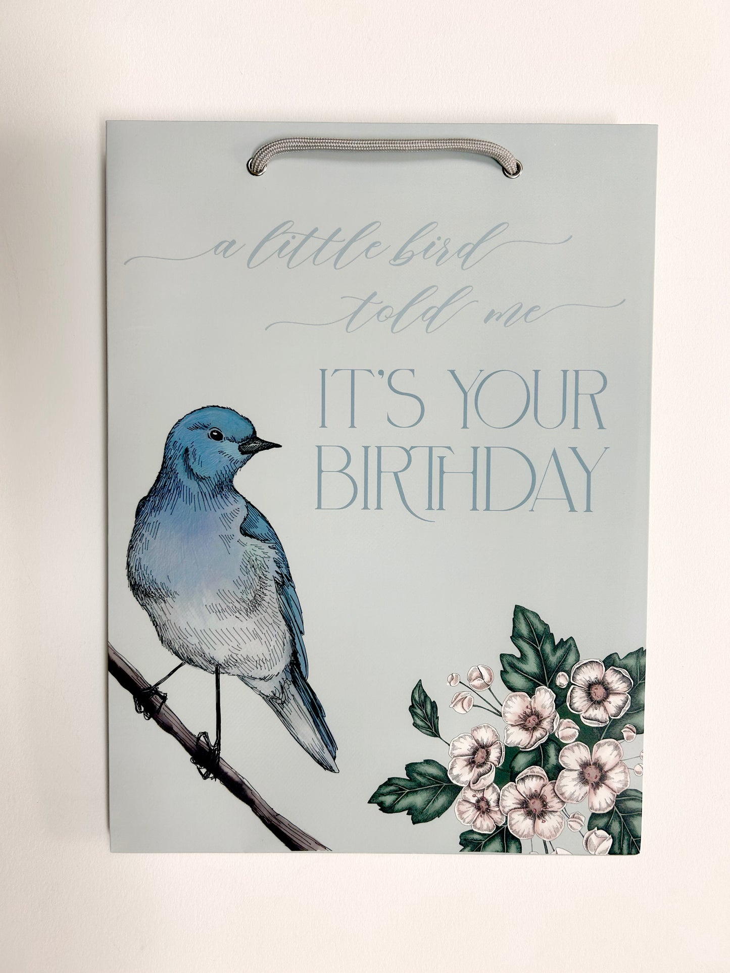  Picture of a flat blue birthday gift bag with florals and a bird that reads "A little bird told me it's your birthday" by Rust Belt Love.