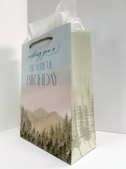 Angled standing up picture of Rust Belt Love's birthday gift bag with mountain and tree scenery that reads "Wishing you a beautiful birthday",