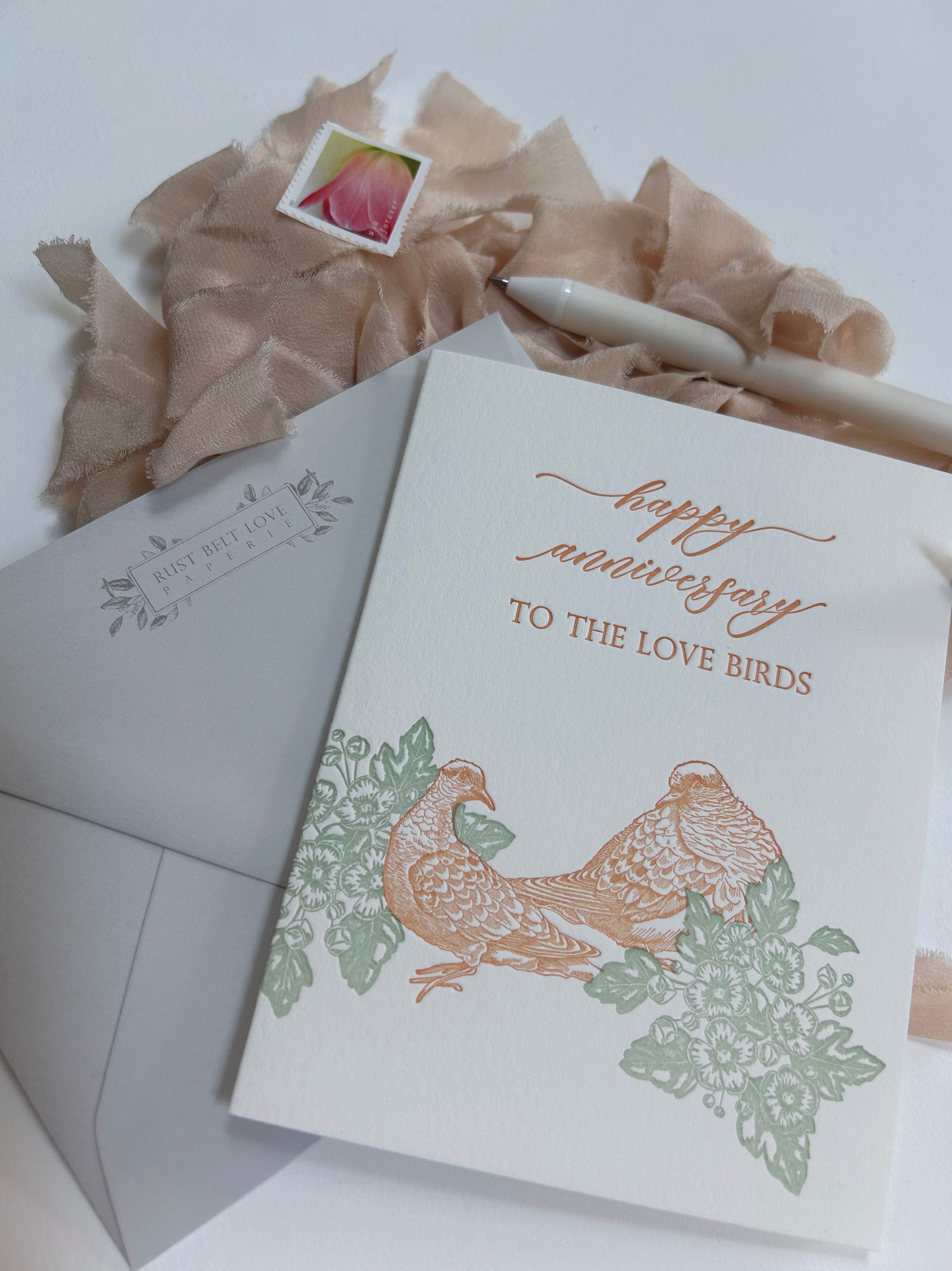 Style shot of letterpress love card with florals and birds that says "Happy anniversary to the love birds" by Rust Belt Love