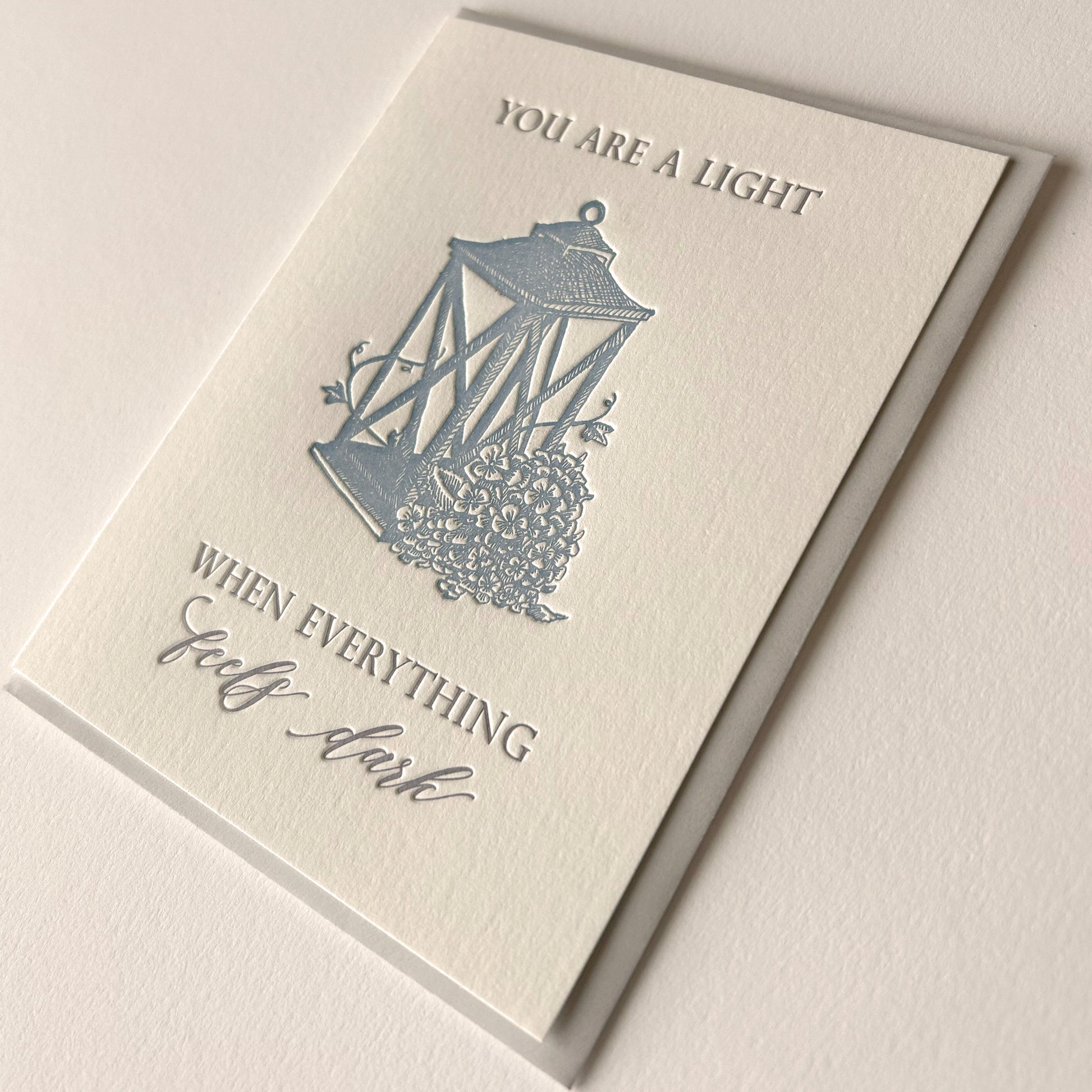 Letterpress love card with a lantern and florals that says " You Are A Light When Everything Feels Dark" By Rust Belt Love