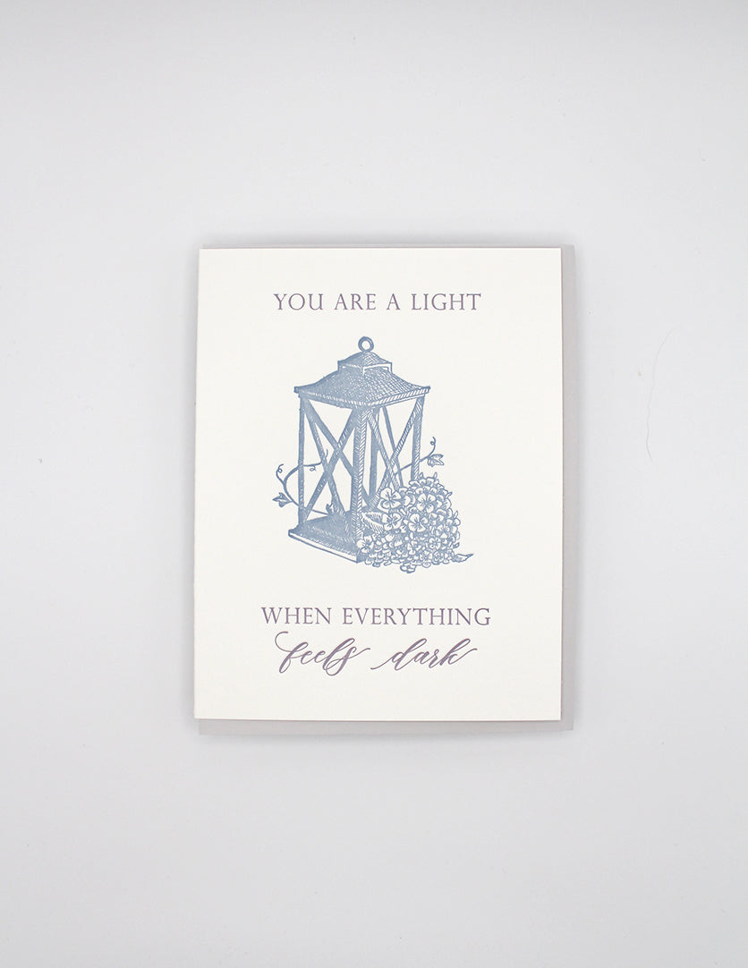 Letterpress love card with a lantern and florals that says " You Are A Light When Everything Feels Dark" By Rust Belt Love