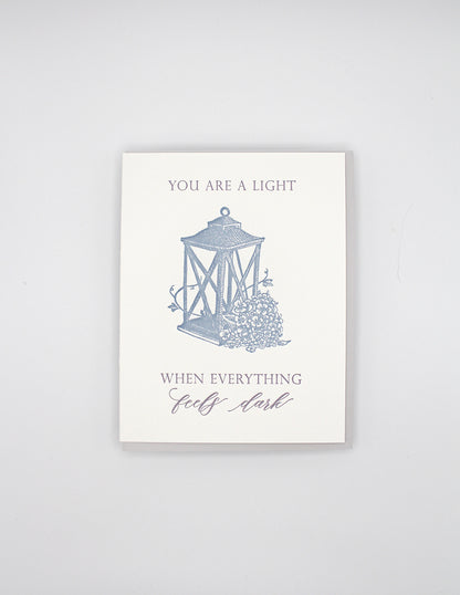 Letterpress love card with a lantern and florals that says " You Are A Light When Everything Feels Dark" By Rust Belt Love