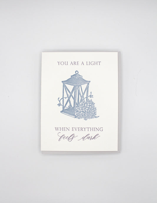 Letterpress love card with a lantern and florals that says " You Are A Light When Everything Feels Dark" By Rust Belt Love