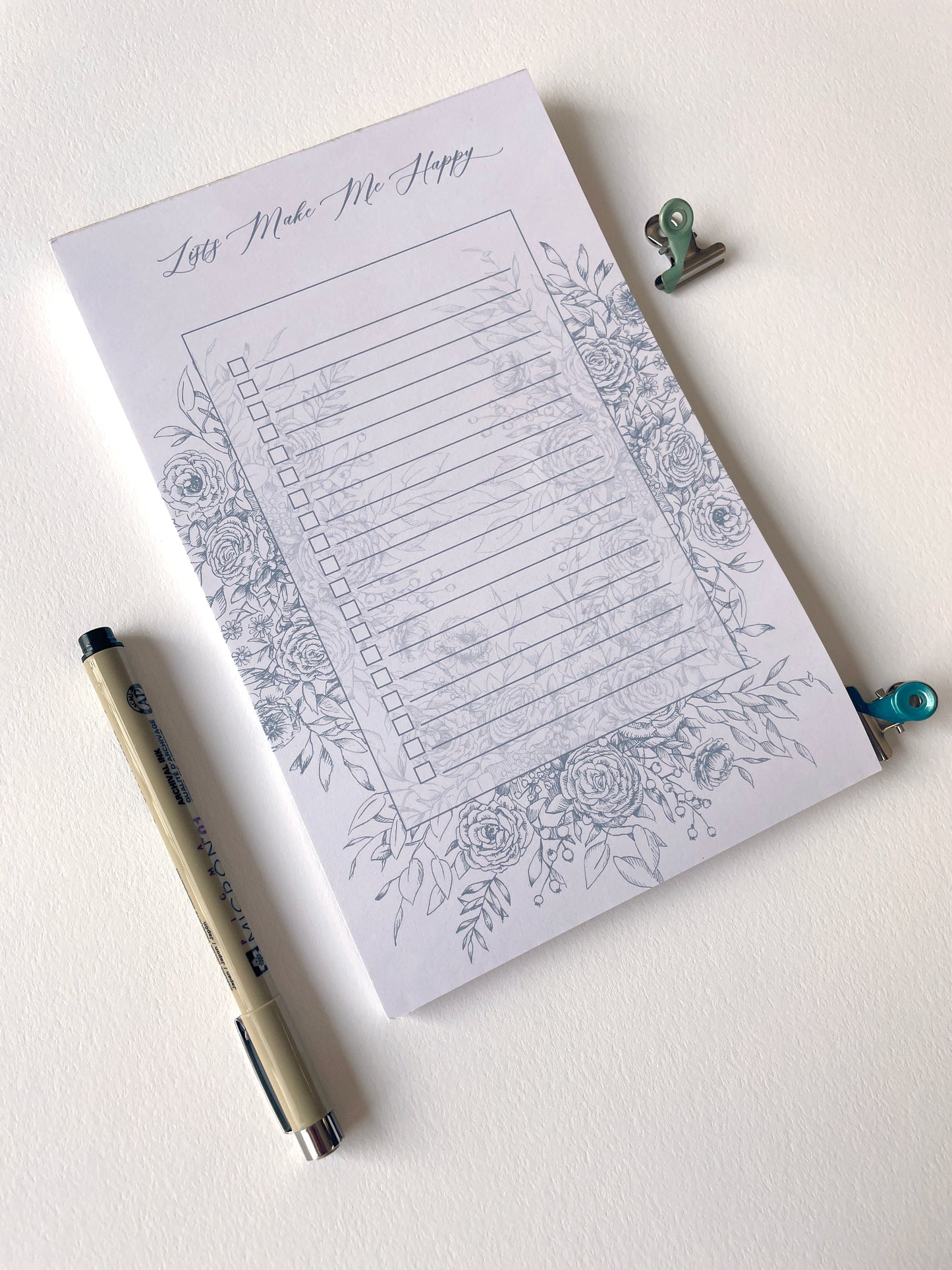 Style shot of 5.5 by 8.5 notepad with lined sheets with blue florals that says "Lists make me happy" by Rust Belt Love