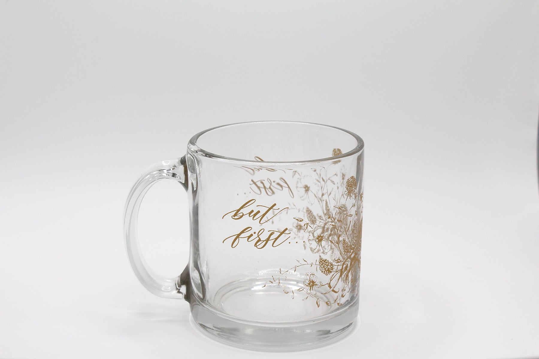 Gold ink on clear glass mug with florals and that says "but first..." by Rust Belt Love