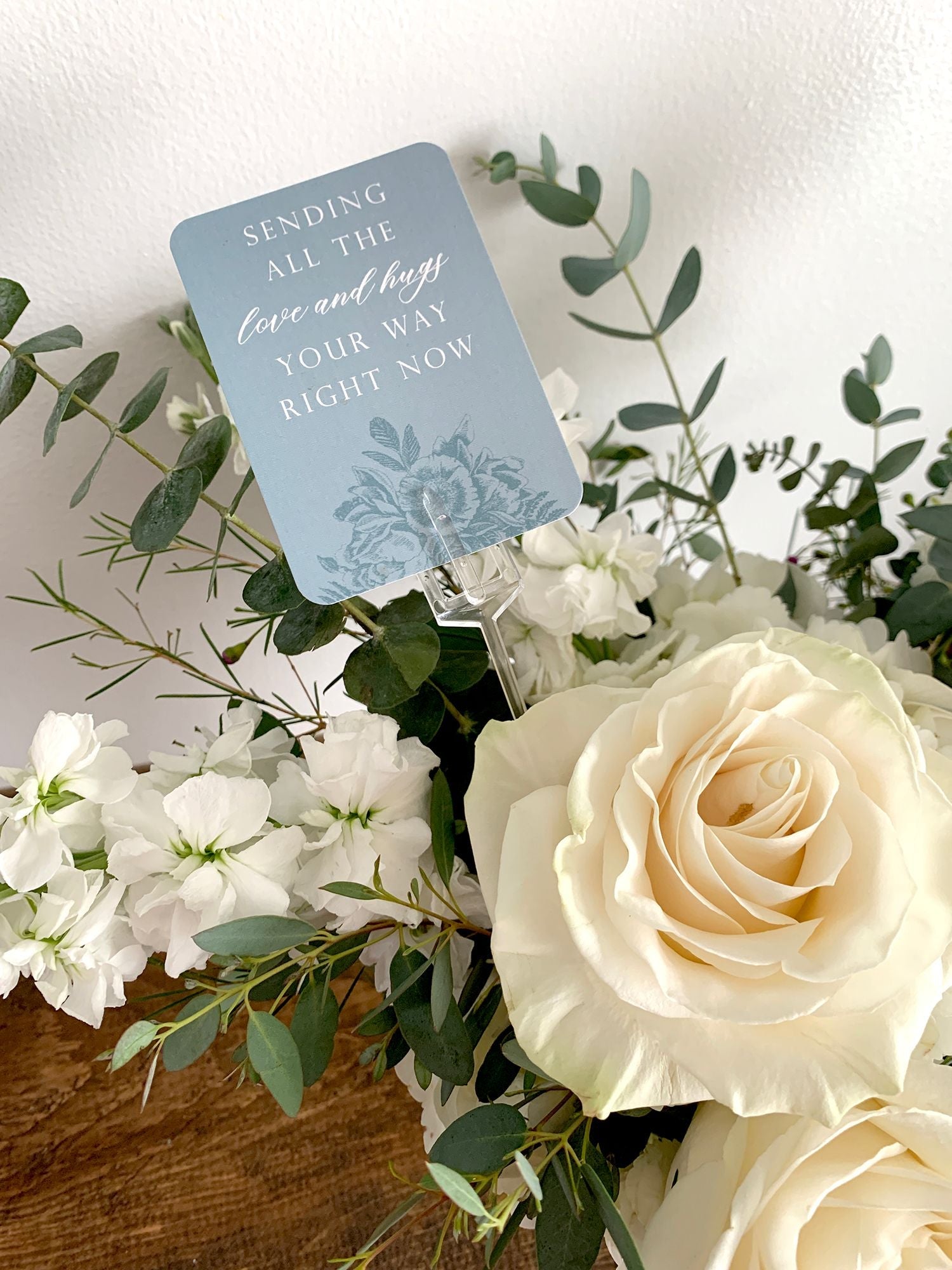 A style shot of "Sending all the love and hugs your way right now" minicard in a bouquet of flowers.